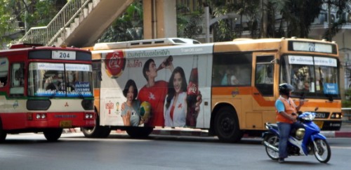 A red / cream regular bus and an orange air-conditioned bus on the streets of Bangkok